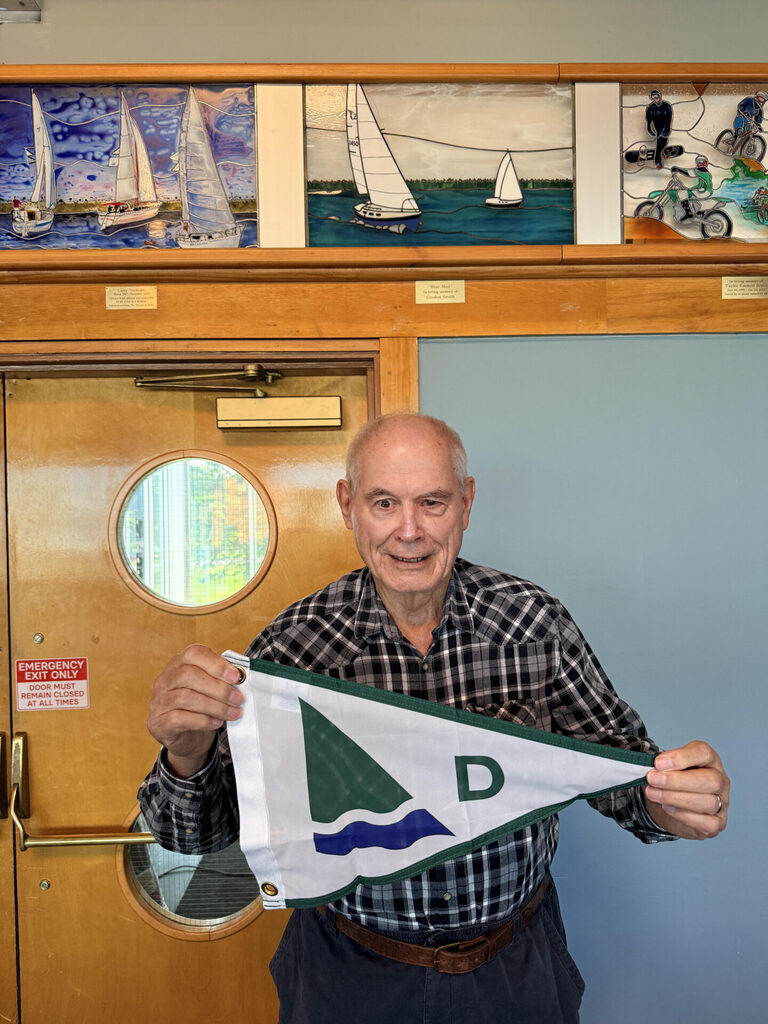 A man holding a burgee (club pennant) below a stained-glass window.