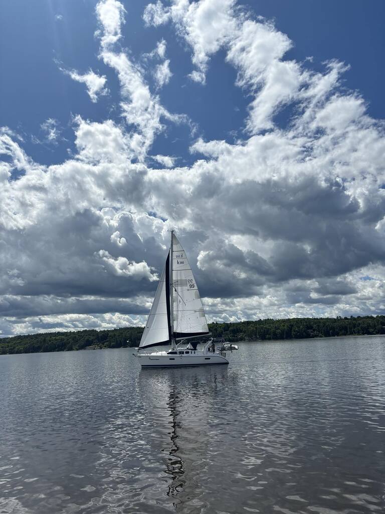 A sailboat in no wind under puffy clouds