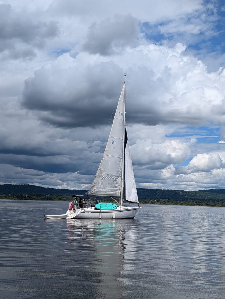A sailboat sailing in little wind with a rainstorm approaching