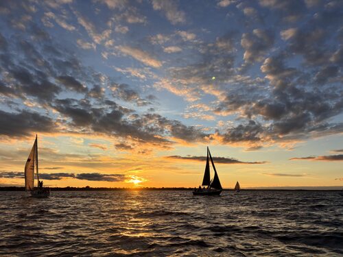 Two sailboats racing under a sunset-lit sky